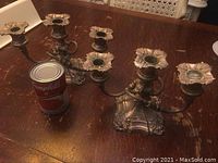 Pair of heavy, ornate Coronet plate E.P. lead candle holders with multiple arms for candles shown on wooden table, alongside a Campbell's soup can for scale reference
