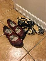 Front view of two pairs of women's shoes, one red Mary Jane style and one black espadrille wedge sandal with ankle straps, both size 9.