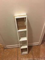 Three white IKEA Lerberg CD/DVD/game shelves shown leaning against a beige wall on tiled floor.