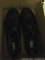 Top view of black Hotter walking shoes inside a cardboard box showing laces and shoe interior with brand name printed.