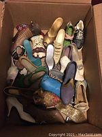 Top-down view showing an open cardboard box filled with various decorative miniature shoe figurines in assorted colors and patterns.