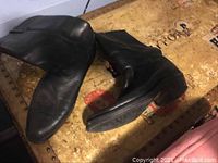 Pair of black leather cowboy boots shown on a wooden surface, side and angled view.