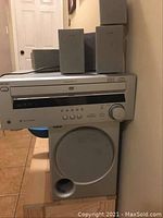 Sony main unit with disc tray, control buttons, and large volume knob with speakers on top and subwoofer below