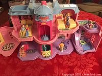 Overview front view of Fisher-Price Little People hotel playset with open rooms, beds, figures, and accessories visible on a red tablecloth.