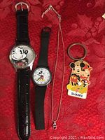 Full lot overview showing two wristwatches (one black leather, one black plastic strap), necklace with pendant, and Mickey Mouse keychain with three characters and name tag.