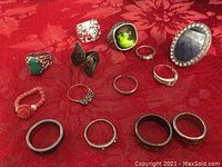 All costume rings displayed on red fabric, showing variety of styles and materials.