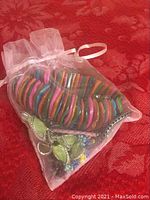 Small translucent white drawstring organza bag holding colorful segmented circular bracelets and green leaf charm bracelet inside