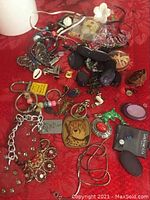 Mixed collection of broken jewelry, pendants, beads, and keychains arranged on a red surface.