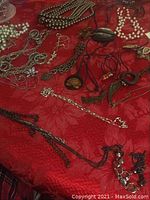 A variety of costume necklaces on a red fabric surface including faux pearls, silver chains, and pendants.