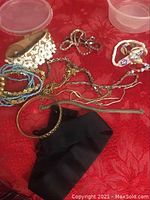 Photo of assorted costume jewelry including bracelets, chokers and several necklaces on a red fabric background, showing various materials and one broken necklace chain.