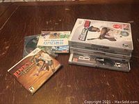 Seven Nintendo Wii games stacked and spread out on a wooden table. Titles include Link's Crossbow Training, Wii Sports, The Beatles Rock Band, Driver Parallel Lines, Guitar Hero III Legends of Rock, Top Spin 3, and MLB 2K8.