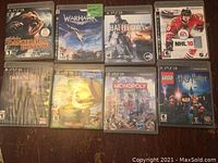 Photo showing eight PS3 game cases arranged on a wooden surface: Cabela's Dangerous Hunts 2013, Warhawk, Battlefield 4, NHL 10, Dark Souls II, The Hobbit, Monopoly Streets, LEGO Harry Potter.