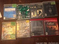 Photo showing eight PS3 game cases arranged in two rows of four. Titles visible include Call of Duty: Black Ops, Dragon Age: Origins, Shadow of the Colossus, Skyrim, Grand Theft Auto IV, Soldier of Fortune: Payback, Oblivion, and Fallout: New Vegas. Games appear to be untested and not checked for completeness.