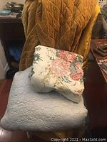 Gold velvet quilt draped over chair with stacked duvet cover and silver satin quilt