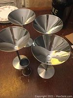 Photo of four steel martini glasses with reflective surface and one small steel shot glass on a wooden surface