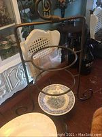 Heavy metal 3-tier cake stand showing the three circular tiers for placing platters or bowls, with floral blue and white ceramic items underneath