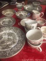 Photo of various plates, bowls, cups, and creamers with brown and red English transferware patterns on a red tablecloth.