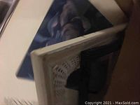 Close-up photo showing corner of a wicker framed painted mirror and a framed floral print.