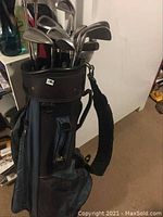 Full view of black and blue golf bag with clubs inside, shoulder strap attached