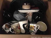 Top-down view of box with ceramic mugs, roaster with lid, shallow dishes and dark glass growlers.