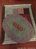 Photo showing two handmade rugs. Oval braided rug placed on top of rectangular patchwork rug.