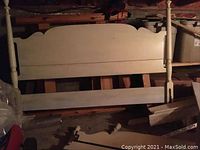 Photo showing double bed headboard, footboard, and rails stacked in a room with low lighting