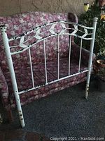 Full view of the rustic single metal headboard showing structure, peeling white paint with black underneath, and decorative leaf design.