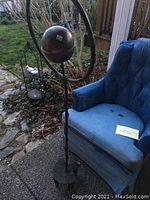 Full view of the copper-colored spherical sprinkler mounted on twisted metal rod with blue chair behind