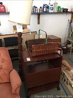 Overall view showing three items: the wooden printer cart, carved floor lamp, and wicker magazine rack in a garage setting.