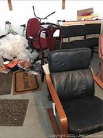 Photo showing black leather cushioned wooden lounge chair in foreground and other chairs in background