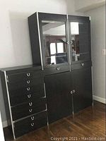 Full front view of the black IKEA cabinet showing the glass doors on the upper unit with drawers to the left and bottom cabinet doors.