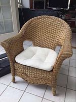 Full view of wicker chair with white cushion seated on tiled floor near glass door.