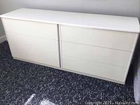 Front view of white dresser with six drawers closed, placed on carpeted floor.