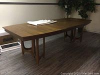 Full view of rectangular walnut veneer dining table with two leaves installed and folded white plastic tablecloth on top