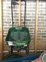 Front view of Scott's Turf Builder EdgeGuard spreader showing green plastic hopper with label, black wheels, and black handle