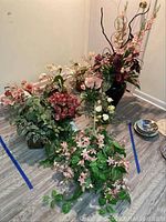 Photo showing nine faux flower arrangements with various colors and designs on a floor with walls.