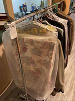 Full view of the rolling metal clothes rack with several garments hanging, showcasing its size and condition.