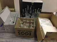 Wide shot showing multiple boxes containing glassware items including pitchers and stemmed glasses.