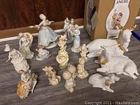Wide view showing entire collection of approximately 18 porcelain and ceramic figurines, including boxed angel, white deer with gold accents, and various small human and animal figures.