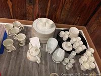 Overview of entire dinnerware set showing plates, cups, saucers, mugs, bowls, egg cups, and tea pot arranged on a wooden table against a wooden wall