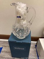 Crystal pitcher on top of its original Marquis Waterford Crystal box, filled with white packing material inside to maintain shape.