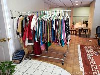 Full view of the metal clothes rack on wheels with hangers and various clothes.