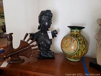 Side view showing the wood carved bird holding utensils, female bust, and large vase on table
