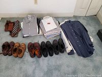 Full view of men's shoes, dress shirts folded, and some dress shirts on hangers along with silk ties placed on carpet