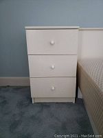 Front view of the off-white nightstand showing three drawers with round knobs and visible surface wear.