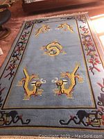 View showcasing the entire rectangular oriental rug, highlighting the yellow dragon motifs and floral border on a light blue background.