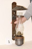 Full front view of the PRR oil lamp mounted on a backplate with hand holding the glass chimney, showing height and overall structure.