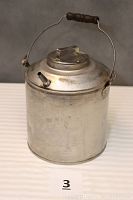 Full view of the cylindrical metal water can with lid, spout, handle and wooden grip, showing the overall item condition and design.