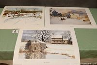 Three large prints depicting snowy rural Chester County scenes placed on a green table, clearly showing two prints on top and one below.