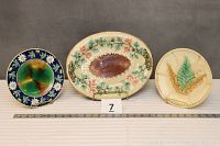 Three Majolica pieces: two round plates flanking an oval platter with floral/leaf motifs.